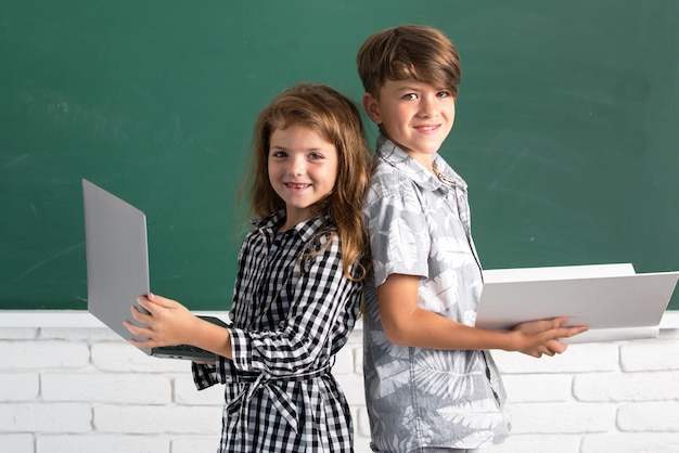 Elementary school kids Portrait of children boy and girl with laptop computer and book at school Kids in class on blackboard