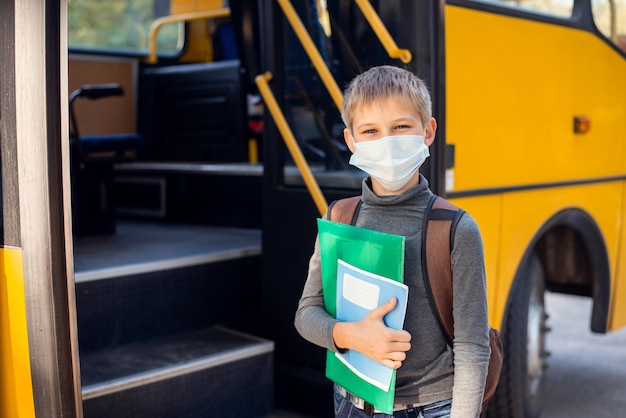 Elementary school learner in facial medical mask going to a bus after the classes