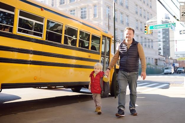 Elementary student hold hands his father near yellow school bus