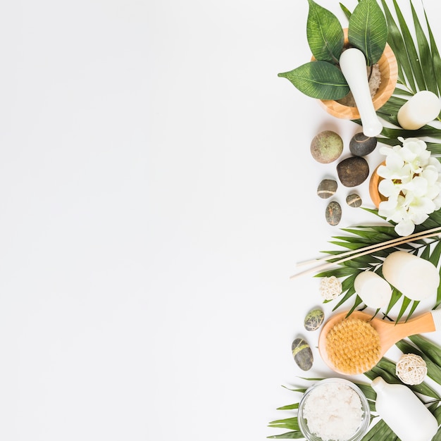 Photo elevated view of flowers; spa stones; leaves; brush and candles on white background