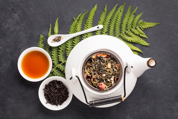 Elevated view of herbal tea and healthy ingredient with fern leaf on black slate background