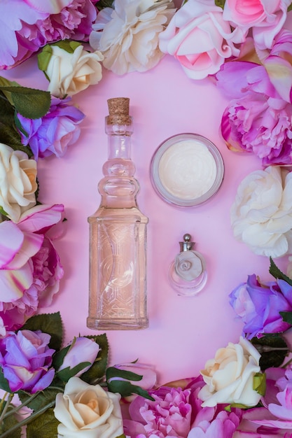 Elevated view of moisturizing cream; essential oil and perfume bottle surrounded with artificial flowers