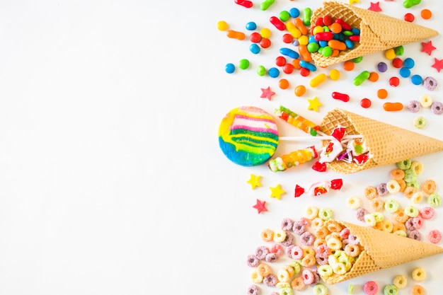 Elevated view of various colorful candies with waffle ice cream cone on white surface