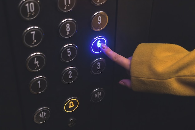 Elevator floor panel in building closeup woman hand touch and press the button on the panel with led...