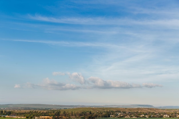 Elongated bands of clouds stretch across the blue sky and under the sky were green fields and hills