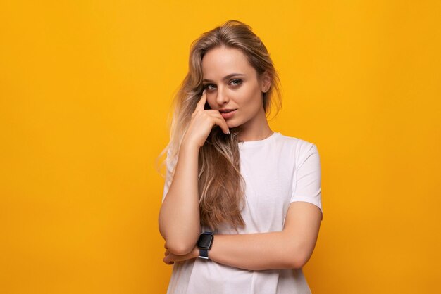 Embarrassed blond girl in a white tshirt on a yellow background with empty space