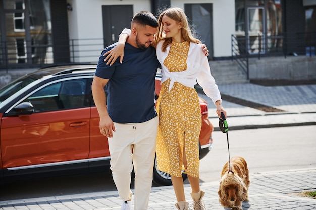 Embracing each other. Lovely couple have a walk together with dog outdoors near the car.