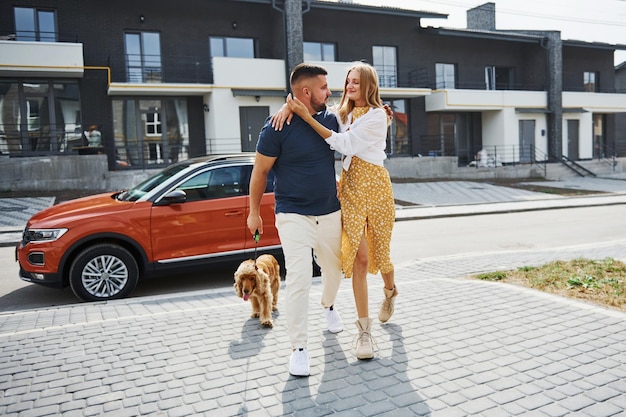 Embracing each other. Lovely couple have a walk together with dog outdoors near the car.