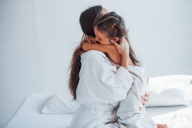 Embracing each other. Young mother with her daugher have beauty day indoors in white room.