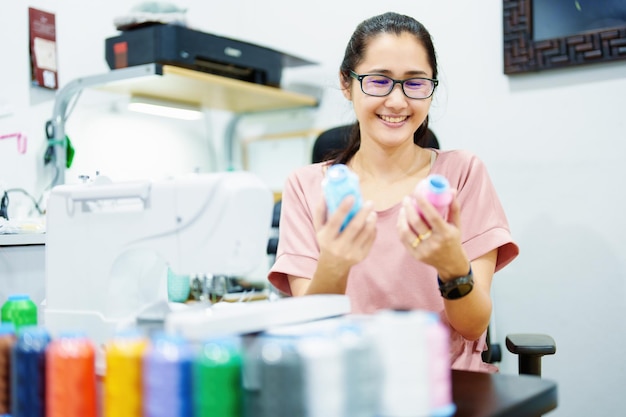 Embroidery handicrafts SME family business Portrait of an Asian female designer picking up sewing threads for Design patterns using automatic embroidery machines according to customer orders