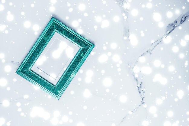 Emerald green photo frame and glowing glitter snow on marble flatlay background for Christmas and winter holidays