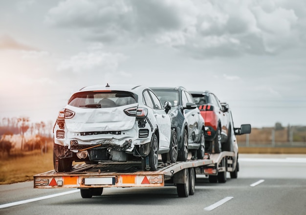 Emergency roadside assistance on the highway side view of the fltabed tow truck with a damaged vehicles after a traffic accident