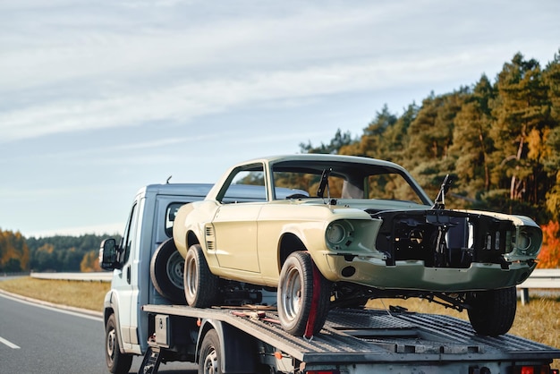 Photo emergency towing service in action on the highway a yellow tow truck transports a damaged car on a flatbed carrier the rear view of the vehicles shows the brake lights and the motion of the traffic