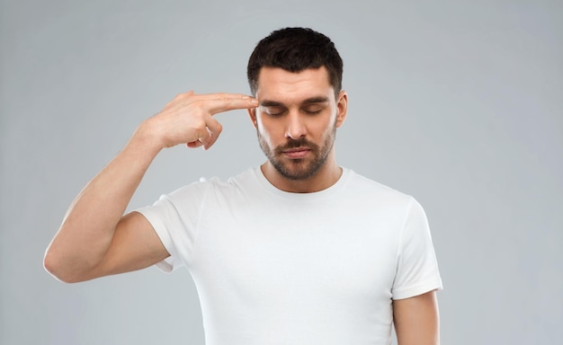 emotion, stress and people concept - man making finger gun gesture over gray background