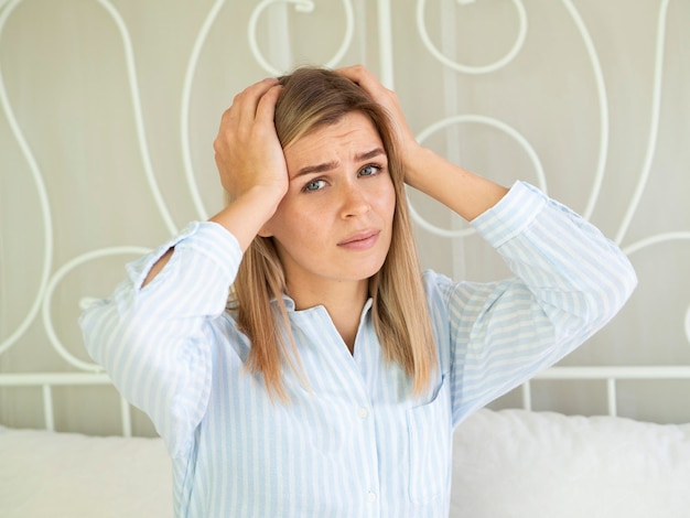 The emotion of suffering. Women with headache severely touch her head, sitting on the bed and looks into the camera. Female migraine.