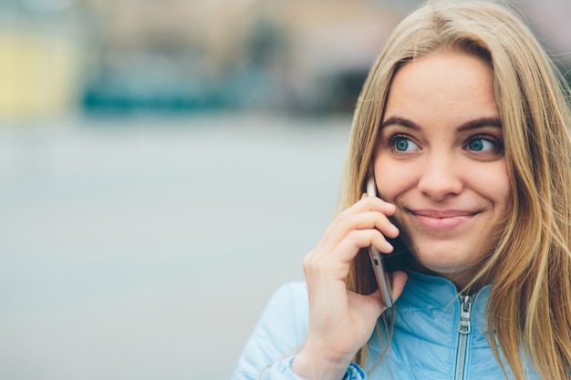 Emotional beautiful blonde talking on the phone outdoors. Female Corrupt faces and indulges in chatting with friends on the cell.