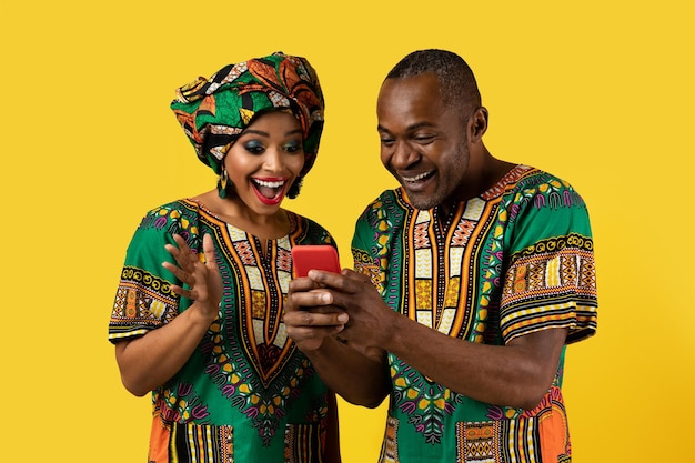 Emotional black couple checking content on cell phone yellow background