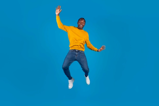 Emotional black man in casual jumping over blue background