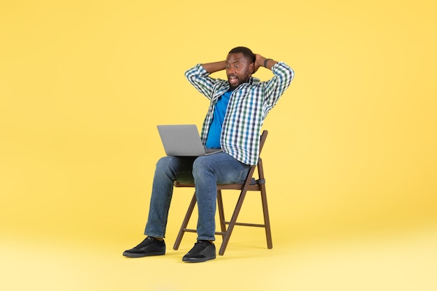 Emotional Black Man Looking At Laptop Sitting Over Yellow Background