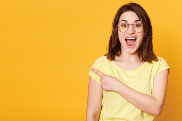 Emotional cheerful young female poses isolated over yellow