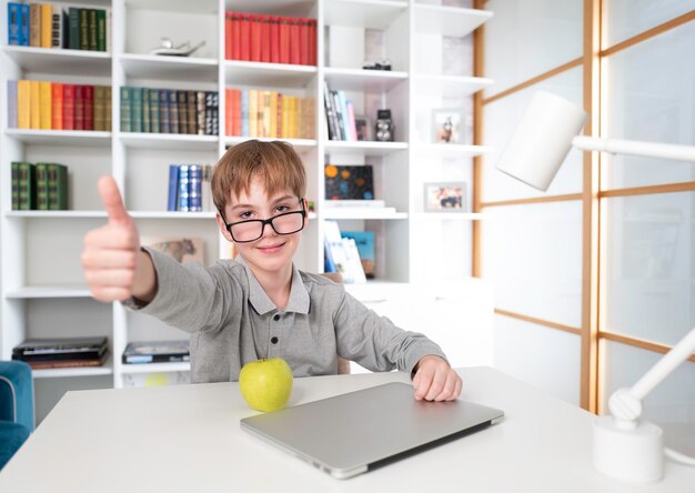 Emotional cute boy studying computer and reading book against the background of white bookshelf