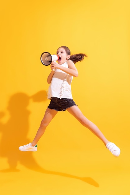 Emotional cute girl kid shouting at megaphone isolated on bright yellow background concept of news