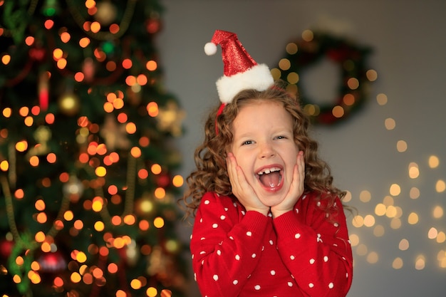 Emotional girl at the Christmas tree waiting for gifts