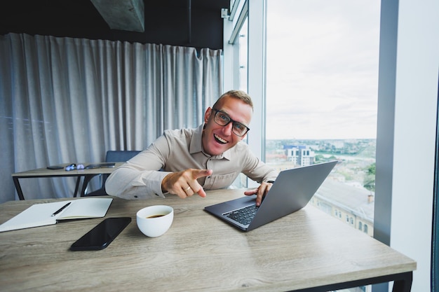 Emotional man looking at the camera at the workplace a man in glasses sitting at a desktop with a computer a student is looking for inspiration for new ideas in an office cafe