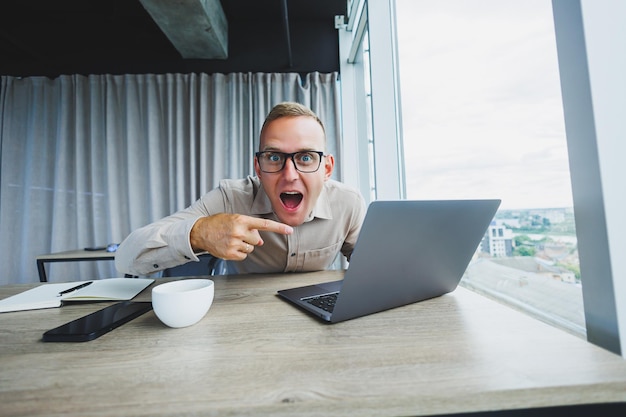 Emotional man looking at the camera at the workplace a man in glasses sitting at a desktop with a computer a student is looking for inspiration for new ideas in an office cafe