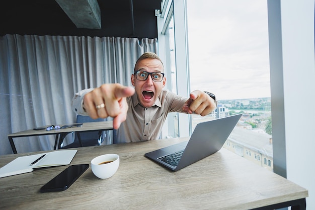 Emotional man looking at the camera at the workplace a man in glasses sitting at a desktop with a computer a student is looking for inspiration for new ideas in an office cafe