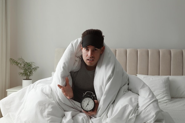 Emotional man with alarm clock in bed Being late because of oversleeping