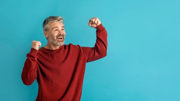 Emotional middle aged man exclaiming and clenching fists on blue