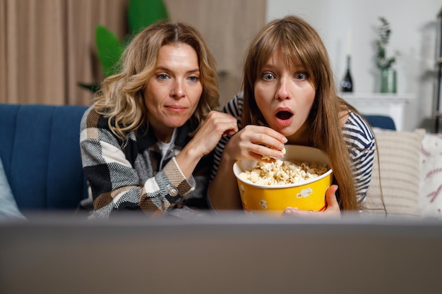 Emotional mother and daughter watching movie on laptop and eating popcorn