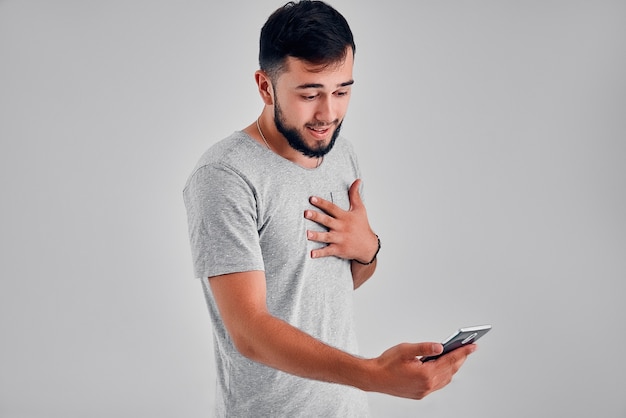 Emotional portrait of beard hipster man screaming while looking on his mobile phone over gray background. Unleashing his emotions.