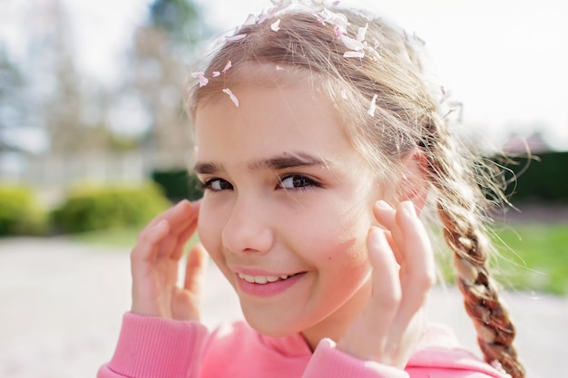 Emotional portrait of girl in pink hoodie with sakura petals on her head and eyelashes spring vibes