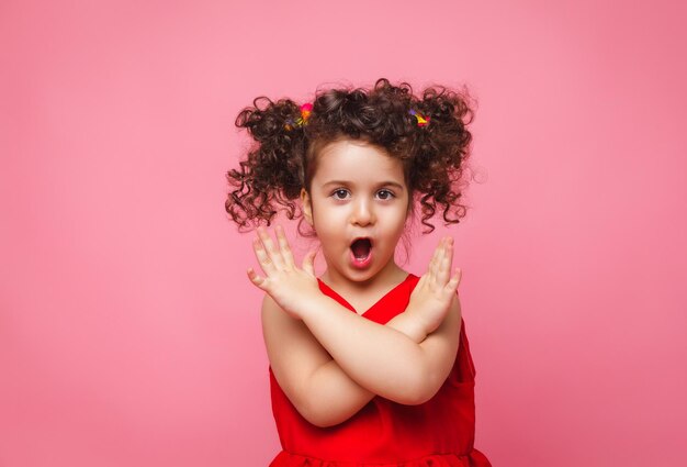 Emotional portrait of a little girl in a red dress on a pink background