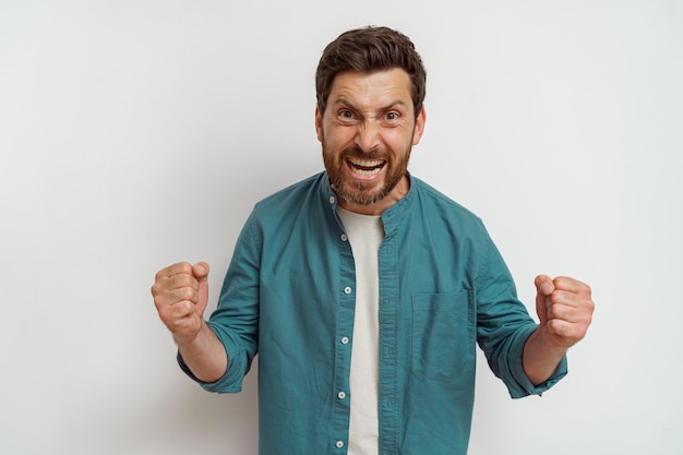 Emotional smiling male fan is standing on white background and screaming with rise arms