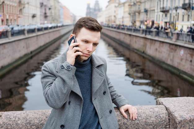 Emotional young man using mobile phone wearing an elegant gray coat stands