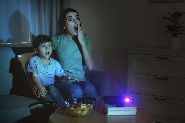 Emotional young woman and her son watching movie using video projector at home Space for text