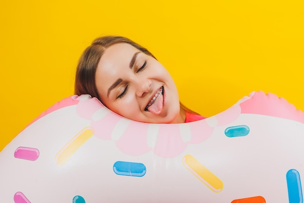 Emotional young woman wearing a pink swimsuit with an inflatable ring isolated on a bright yellow background Summer hotel pool sea vacation sun tanning concept