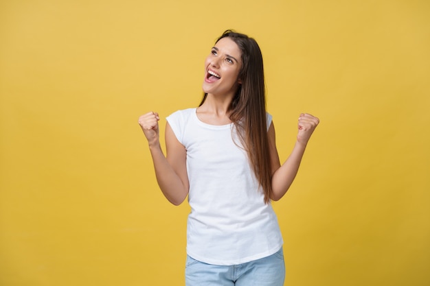 Emotions, expressions, success and people concept - happy young woman or teenage girl celebrating victory isolated over yellow background.