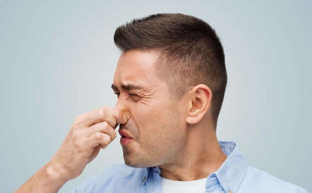 emotions, gesture and people concept - man wrying of unpleasant smell and closing his nose over gray background