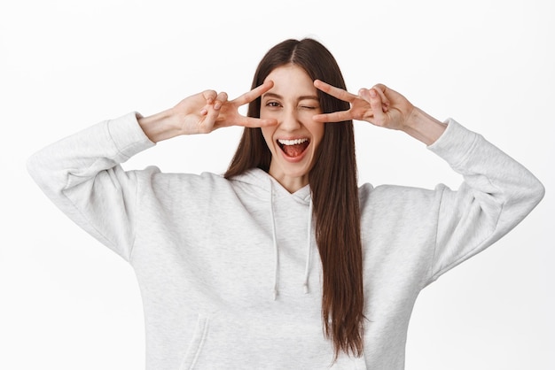 Emotions and lifestyle Happy girl shows vsigns peace disco over eyes winking and smiling positive staying on bright side feeling upbeat standing against white background