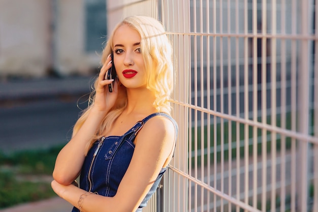 Emotive blond attractive girl in sunglasses with phone in summer sunshine urban