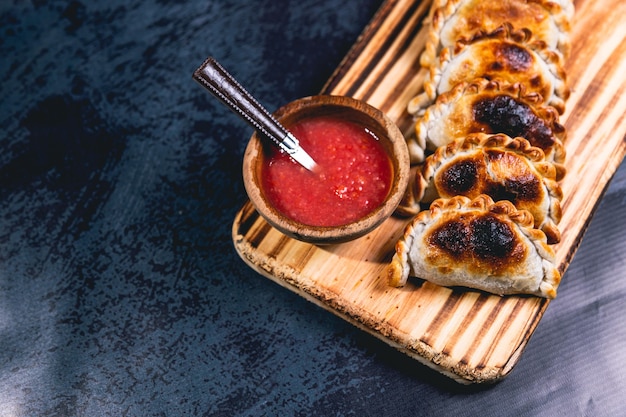 Empanadas on a wooden plate and hot sauce