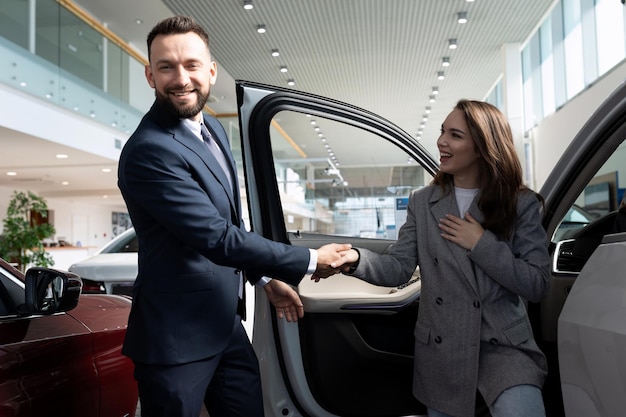 An employee of a car dealership helps a young woman with a choice of a new car