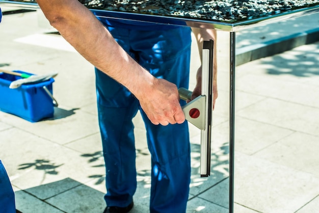 An employee of a cleaning company washes a glass scraper mirror cleaning the park on a summer day male hands