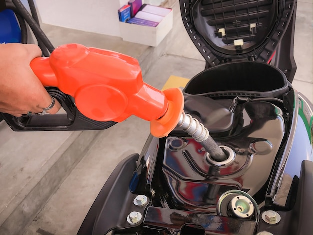 employee holding the fuel dispenser and adding benzyl fuel to the motorcycle's fuel tank.