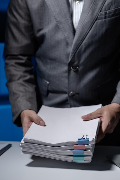 An employee was tidying up a pile of documents piled on his desk before returning home from work A businessman is tidying up his desk because there are many documents he has completed