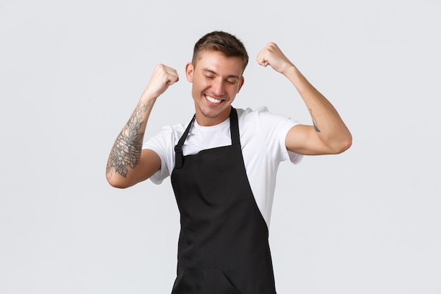 Employees, grocery stores and coffee shop concept. Portrait happy pleased male student got part-time job, dancing from satisfaction, triumphing, fist pump and smiling, barista celebrating good news